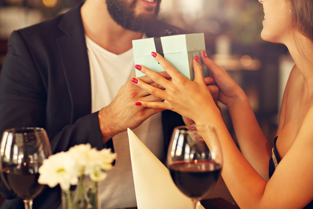 woman with red nails gives bearded man a gift box.